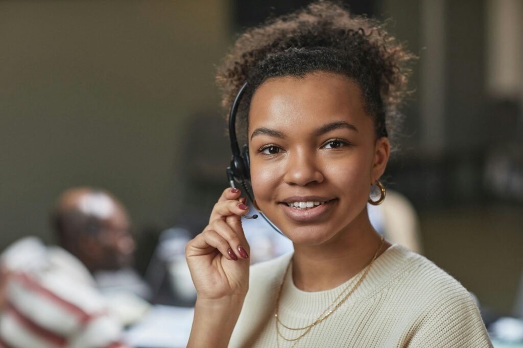 pexels-photo-7689884-7689884 Friendly woman in a call center environment, wearing a headset and smiling.